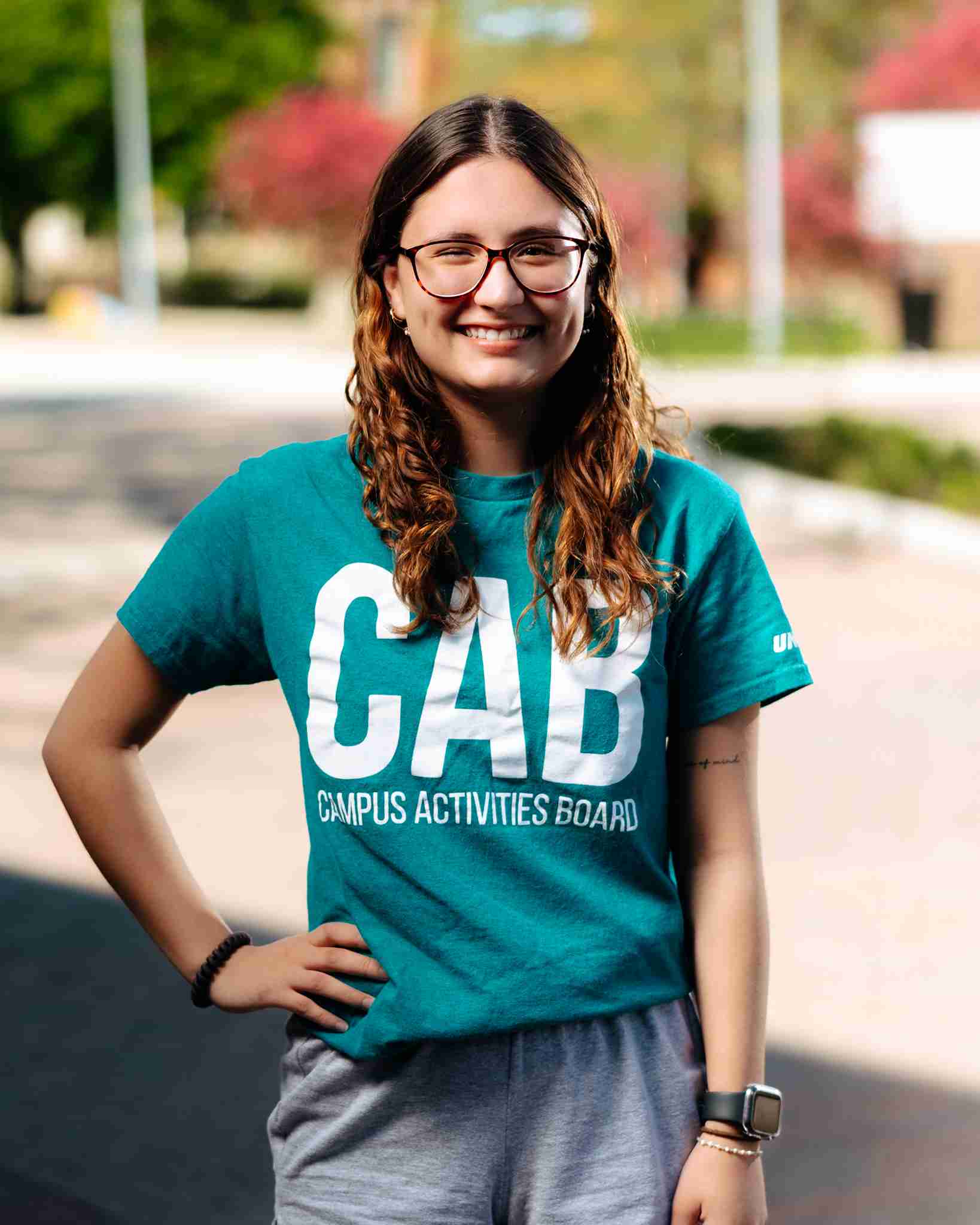Girl with brown hair standing outside wearing teal shirt