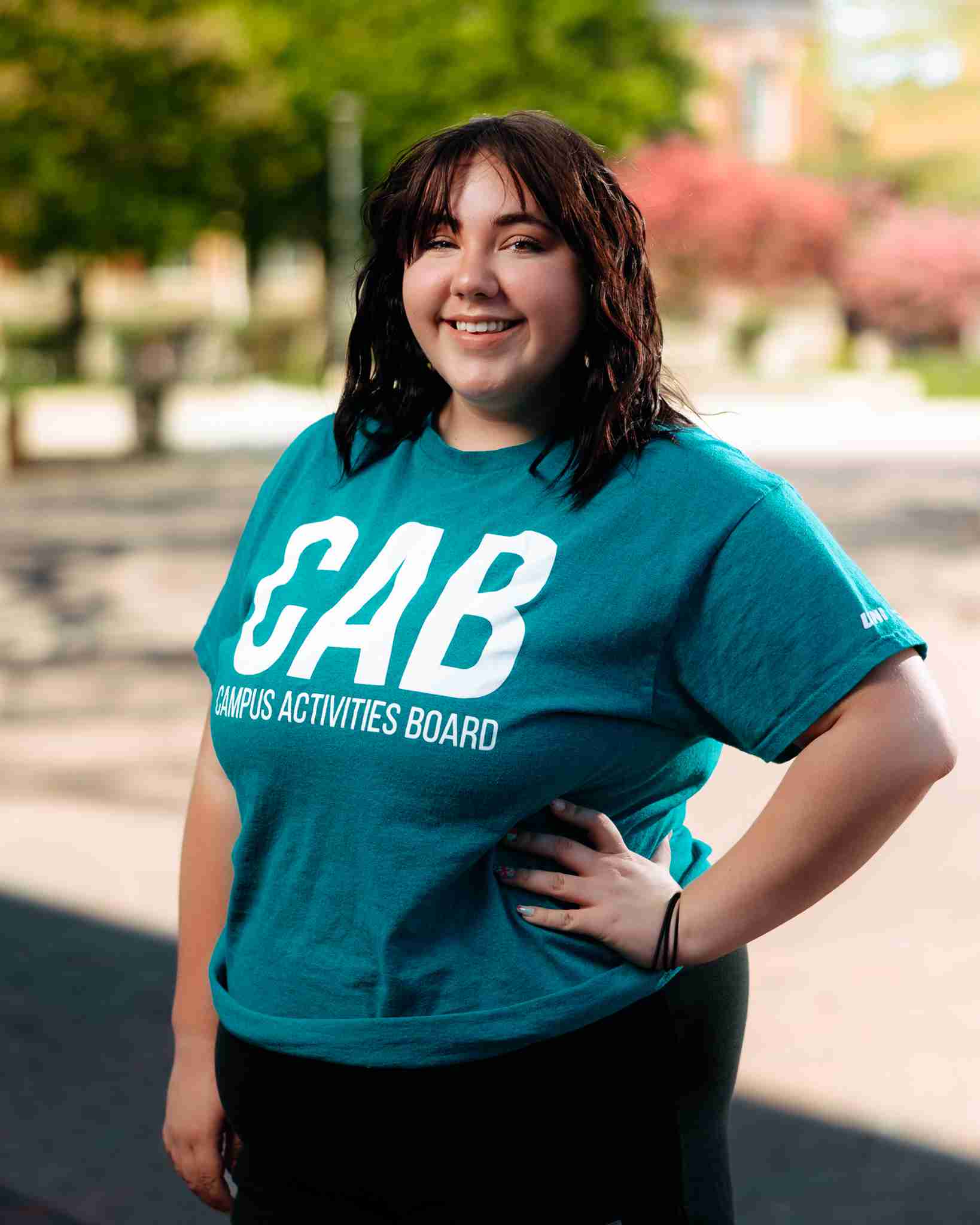 Girl with brown hair standing outside wearing teal shirt