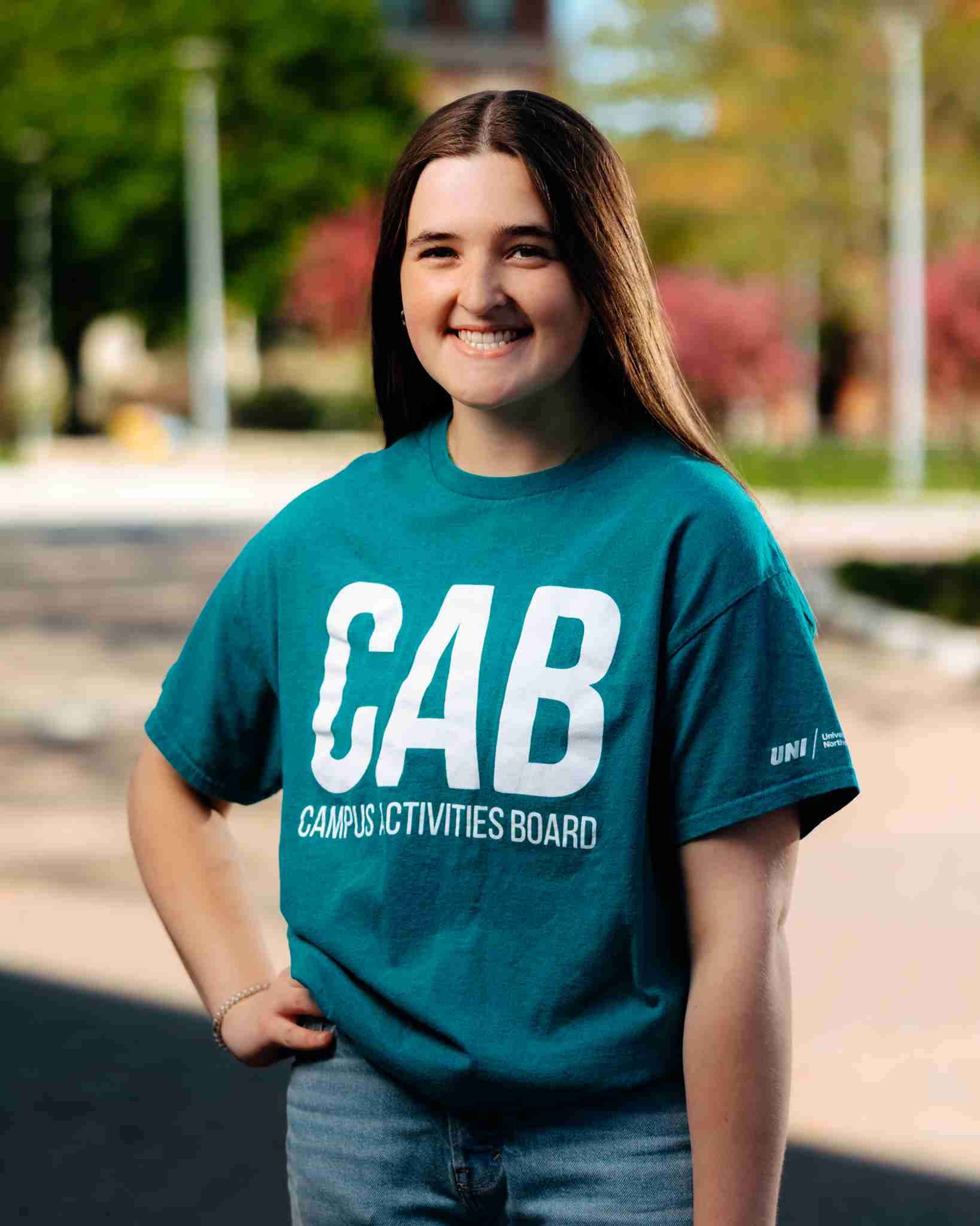 Girl with brown hair standing outside wearing teal shirt