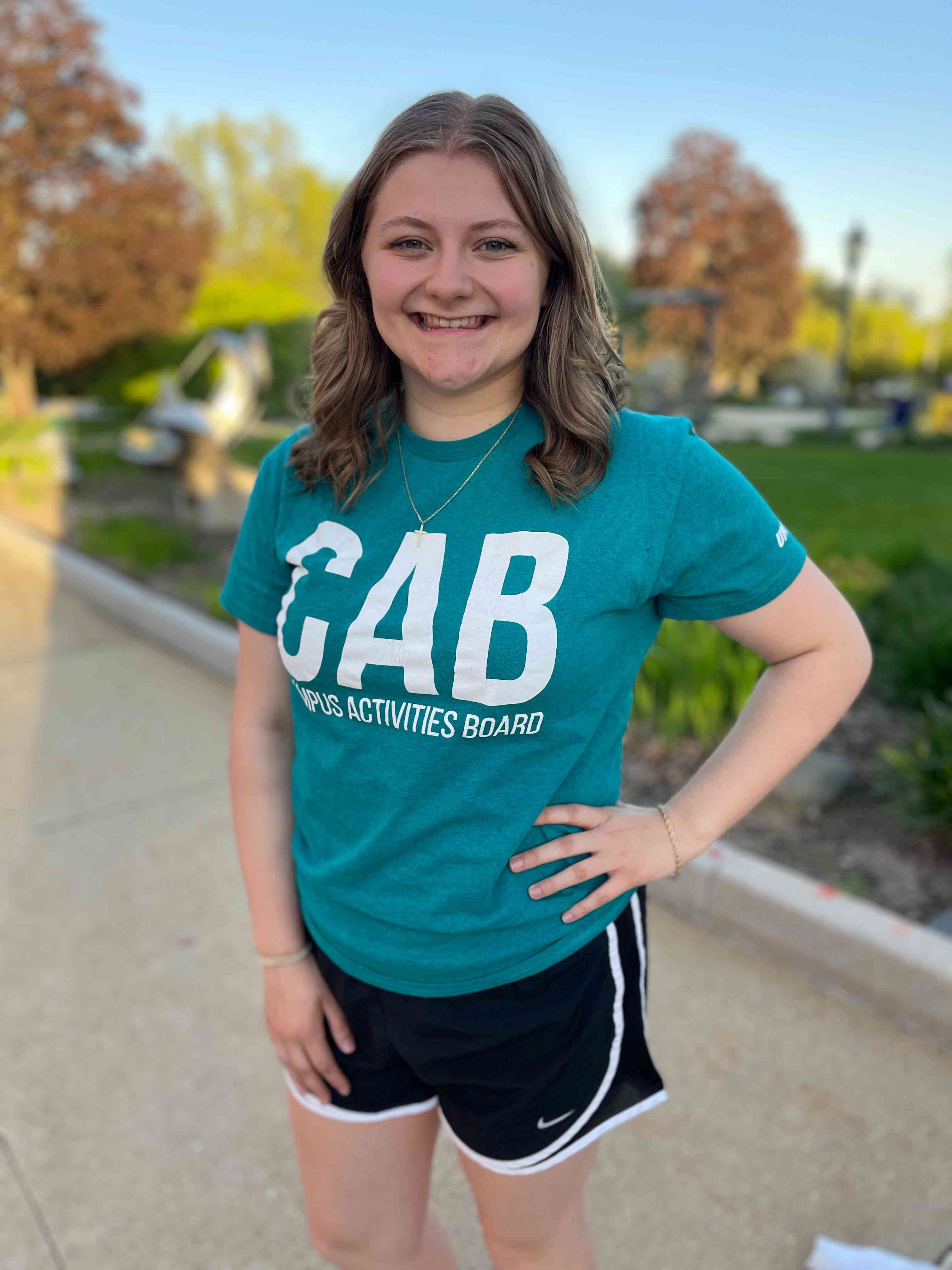Girl with brown hair standing outside wearing teal shirt