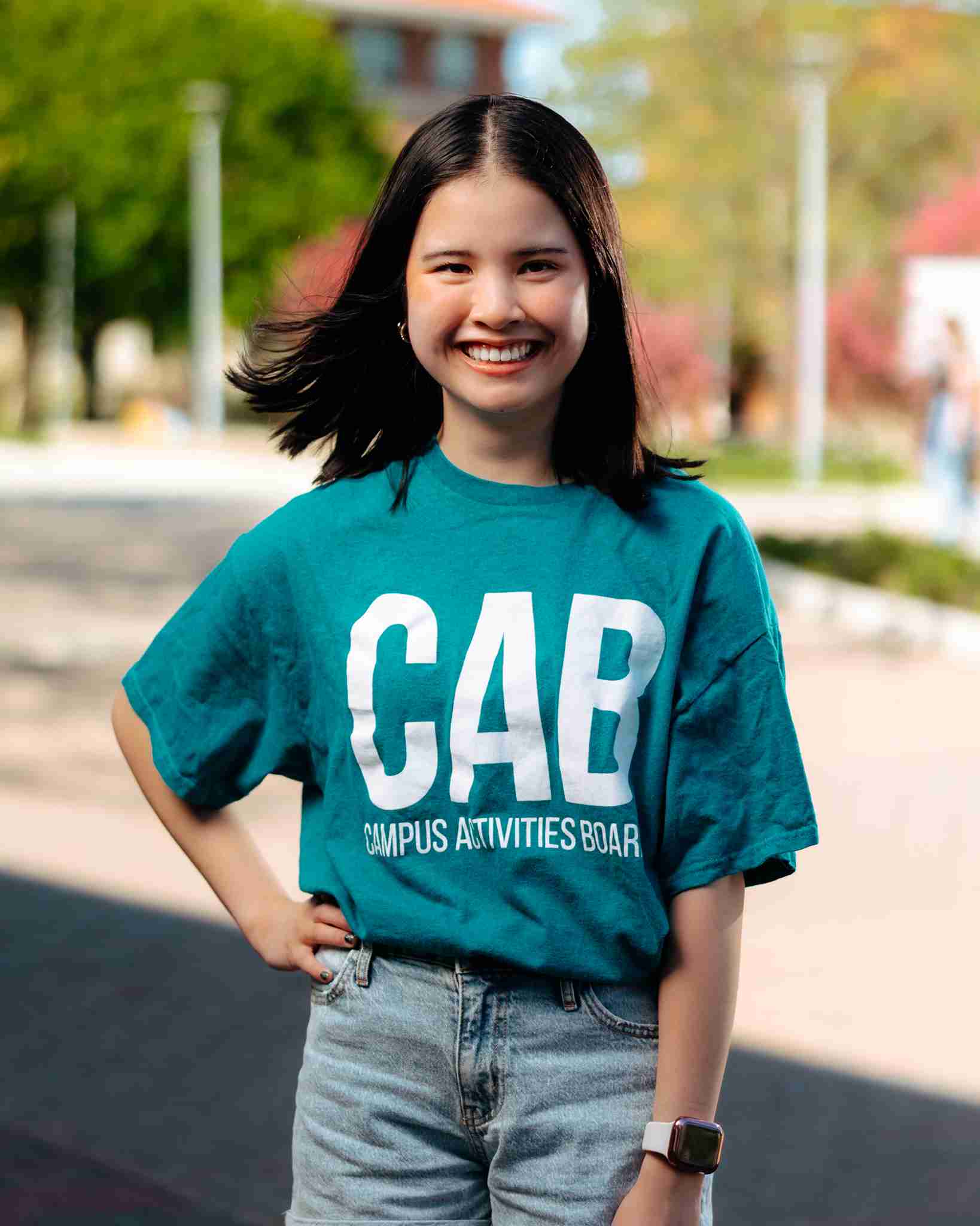 Girl with brown hair standing outside wearing teal shirt