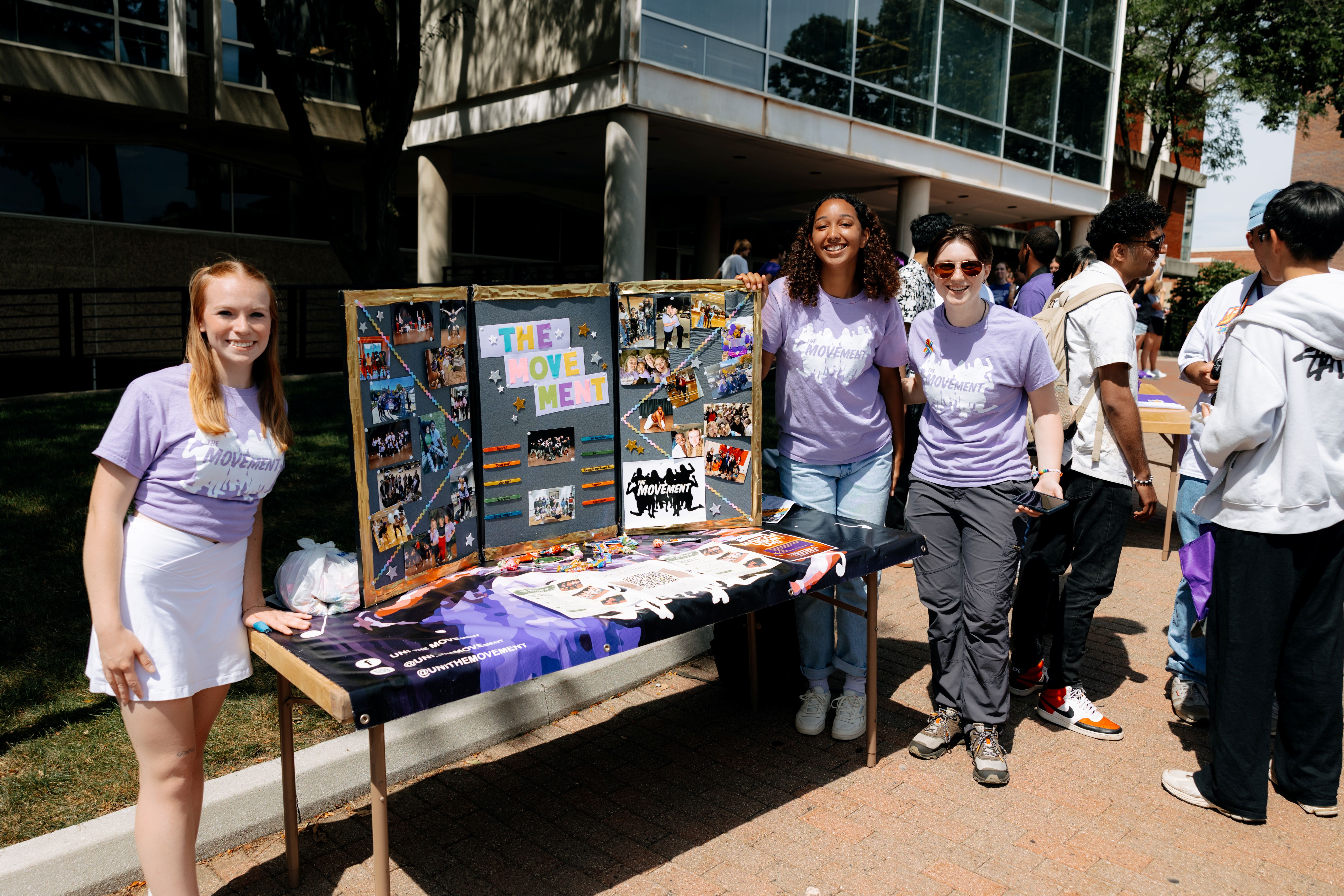 Three students standing around a poster board display on top of a table.
