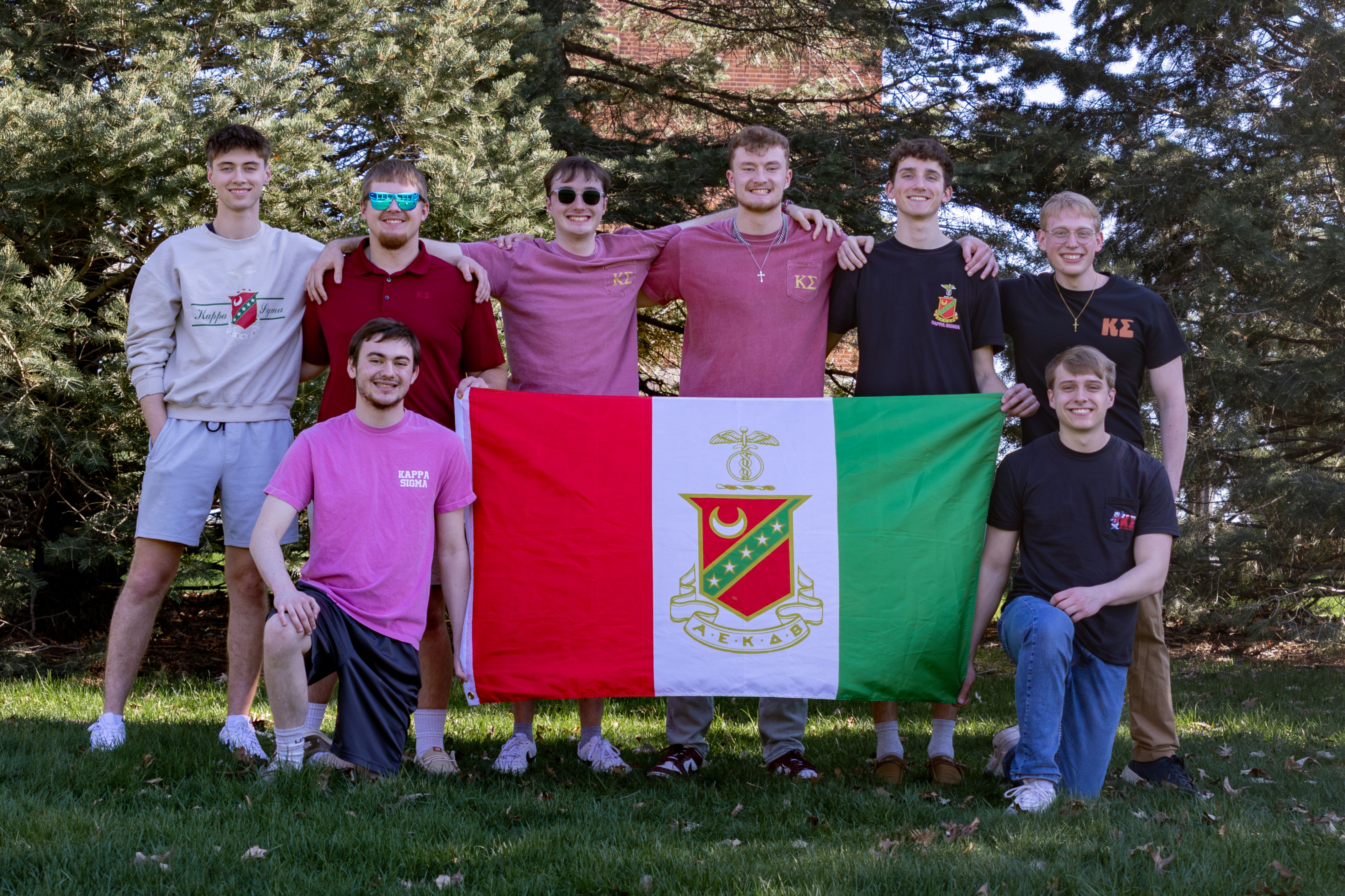 Eight men posing around fraternity flag
