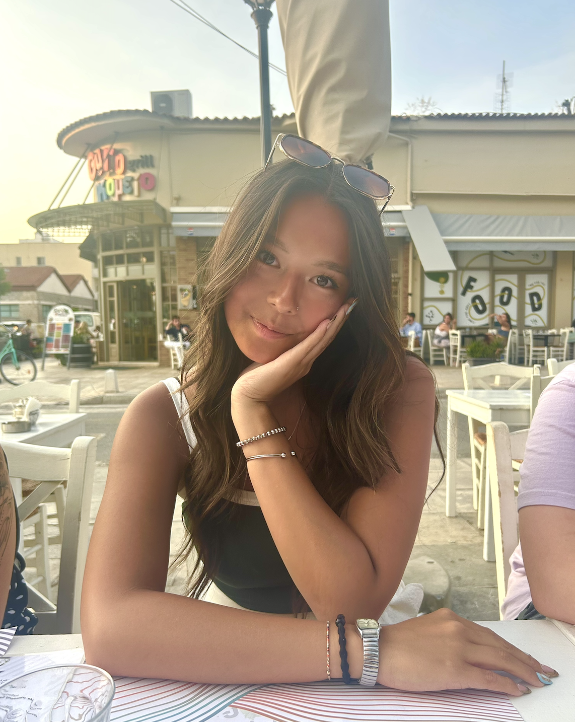 Young woman with dark hair sitting down at a restaurant patio posing for the camera. 